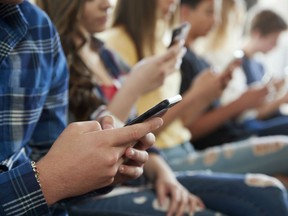 High school students using their phone.  Starting in September, Ontario will ban cell phones in class, in a move some say is to deflect attention from criticism of autism funding.