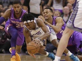 Sacramento Kings guard De'Aaron Fox, center, dives for the ball between Phoenix Suns' Mikal Bridges, left, and Elie Okobo during the first quarter of an NBA basketball game Saturday, March 23, 2019, in Sacramento, Calif.