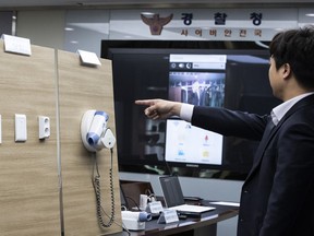 In this Wednesday, March 20, 2019 photo, a police officer demonstrates mini-spy cameras installed at hair dryer, as he is shown on a screen, center rear, at a police station in Seoul, South Korea. South Korean police on Thursday, March 21, 2019, say they've arrested four people on suspicion of secretly filming about 1,600 guests in hotel rooms and posting or streaming the footage on the internet. The Korean National Police Agency said Thursday the four men are accused of installing mini-spy cameras in TV set-top boxes, hair dryers or electrical outlets in 42 rooms in 30 hotels throughout South Korea.