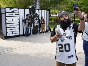 San Antonio Spurs fan Mike Belfort takes a photo in front of a sign thanking Spurs legend Manu Ginobili before an NBA basketball game against the Cleveland Cavaliers, Thursday, March 28, 2019, in San Antonio. Ginobili's jersey will be retired after the game.