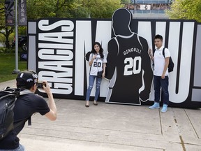 San Antonio Spurs fans pose for a photo in front of a sign thanking Spurs legend Manu Ginobili before an NBA basketball game against the Cleveland Cavaliers, Thursday, March 28, 2019, in San Antonio. Ginobili's jersey will be retired after the game.