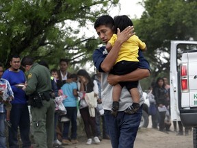 In this Thursday, March 14, 2019, photo, Jose Fermin Gonzalez Cruz holds his son, William Josue Gonzales Garcia, 2, as they wait with other families who crossed the nearby U.S.-Mexico border near McAllen, Texas, for Border Patrol agents to check names and documents. Immigration authorities say they expect the ongoing surge of Central American families crossing the border to multiply in the coming months.