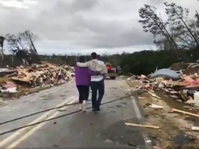 People walk amid debris in Lee County, Ala., after what appeared to be a tornado struck in the area Sunday, March 3, 2019. Severe storms destroyed mobile homes, snapped trees and left a trail of destruction amid weather warnings extending into Georgia, Florida and South Carolina, authorities said. (WKRG-TV via AP)