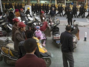FILE - In this Nov. 5, 2017, file photo, residents watch a convoy of security personnel armed with batons and shields patrol through central Kashgar in western China's Xinjiang region. China says on Monday, March 18, 2019 it has arrested nearly 13,000 people it describes as terrorists in the traditionally Islamic region of Xinjiang since 2014 and broken up hundreds of "terrorist gangs." The figures were included in a government report on the situation in the restive northwestern territory that seeks to respond to growing criticism over the internment of an estimated 1 million members of the Uighur (WEE-gur) and other predominantly Muslim ethnic groups.