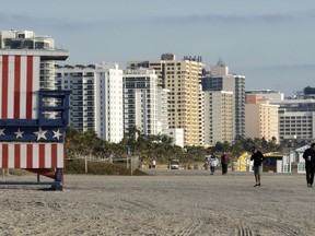 In this photo taken on Jan. 21, 2019, people walk past a lifeguard booth painted in the colors of an American flag on a beach in Miami Beach, Fla. The Miami area is popular among Russians not only for its tropical weather but also because of the large Russian-speaking population. Sunny Isles Beach, a city just north of Miami, is even nicknamed "Little Moscow".