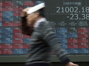 A man walks in the rain past an electronic stock board showing Japan's Nikkei 225 index at a securities firm in Tokyo Monday, March 11, 2019. Shares were mixed in Asia on Monday as investors awaited further developments in trade talks between the U.S. and China.