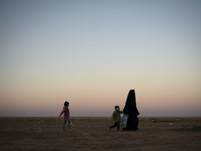 A woman walks with her children at a U.S.-backed Syrian Democratic Forces (SDF) screening area after being evacuated out of the last territory held by Islamic State militants, in the desert outside Baghouz, Syria, Friday, March 1, 2019.