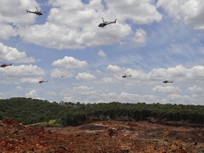 FILE - In this Feb. 1, 2019 file photo, helicopters hover over an iron ore mining complex to release thousands of flower petals, in homage of those who were killed or went missing after a mining dam collapsed a week prior in Brumadinho, Brazil. In late March 2019, firefighters in Brazil are still looking for 93 people who remain missing two months after the dam containing mining waste collapsed.