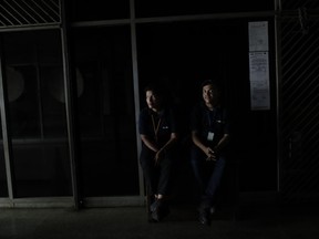 People wearing El Universal newspaper uniforms sit inside a darkened office building during a power outage in Caracas, Venezuela, Monday, March 25, 2019. The subway suspended service because of the power cuts Monday, as local media reported outages in at least six states.