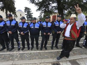 A protester dressed in traditional clothing flashes the victory sign in front of Albanian policemen guarding the parliament building in Tirana, on Thursday, March 28, 2019. Albanian opposition protesters have repeated attempts to enter the parliament by force in their protest asking for the government's resignation and an early election.