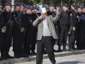 A protester flashes the victory sign in front of Albanian policemen guarding the parliament building as opposition supporters gather to take part in an anti-government rally , in Tirana , Albania, Tuesday, March 5, 2019. The opposition demanded the government step down, claiming it's corrupt and has links to organized crime.
