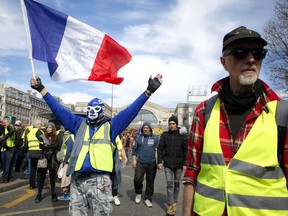 A masked protester waves the French flag as French yellow vest protesters rally to support an older woman activist injured in a confrontation with police, Saturday, March 30, 2019, in Paris. The demonstrators are undeterred by protest bans or repeated injuries in 20 weeks of demonstrations, marching again Saturday in Paris, Bordeaux and other cities to keep pressing President Emmanuel Macron to do more to help working classes, redesign French politics _ or step down altogether.