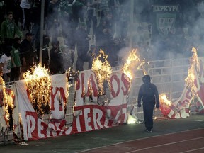 Fans burn a banner in front of stands during a Greek Super League soccer match inside the Athens' Olympic stadium, in Athens, Sunday, March 17, 2019. The derby between Greek league archrivals Panathinaikos and Olympiakos has been abandoned after a small number of Panathinaikos fans clashed with police outside Athens' Olympic stadium. (InTime Sports via AP)