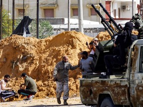 This April 10, 2019 photo taken near Tripoli shows fighters taking cover behind a dirt barrier by an improvised pickup truck mounted with turrets, as pro-government forces clash with forces loyal to strongman Khalifa Haftar.