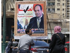 People walk past a banner supporting proposed amendments to the Egyptian constitution with a poster of Egyptian President Abdel-Fattah el-Sissi in Cairo, Egypt, Tuesday, April 16, 2019. Egypt's parliament was holding its last debate Tuesday on proposed amendments to the constitution that could see President Abdel-Fattah el-Sissi remain in power until 2030. Arabic reads, "do the right thing, yes to the developments, stability and amendments to the the constitution".