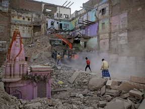 In this March 19, 2019, photo, locals walk past workers demolishing a house at the site of a proposed grand promenade connecting the sacred Ganges river with a centuries-old temple dedicated to Lord Shiva, in Varanasi, India. A project in the ancient Indian city of Varanasi dreamed up by Prime Minister Narendra Modi shows the master political marketer's penchant for symbolism as political strategy in elections that begin this month.