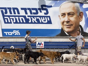 Dog walkers argue as they pass by an election campaign billboard shows Israeli Prime Minister Benjamin Netanyahu in Tel Aviv, Israel, Monday, April 8, 2019. Israel's election on Tuesday boils down to a referendum on Prime Minister Benjamin Netanyahu, who has dominated the country's politics for the better part of three decades. The Hebrew writing say "Strong Likud, Strong Israel.
