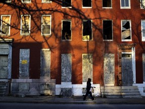 FILE-In this March 30, 2013 file photo, a woman walks past blighted row houses in Baltimore. New annual estimates from the U.S. Census Bureau show that Baltimore is continuing to shed inhabitants. Census data released Thursday, April 18, 2019 shows that Maryland's biggest city lost an estimated 7,346 citizens during the 12 months that ended July 1.