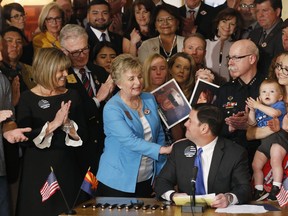 Arizona Republican Gov. Doug Ducey, seated, smiles as he gets a pat on the shoulder from bill sponsor Sen. Kate Brophy McGee, third from left, R-Phoenix, as the governor signs into law a distracted driving bill during a ceremony at the Arizona Capitol Monday, April 22, 2019, in Phoenix. Arizona becomes the 48th state to ban texting and the 18th to ban any hand-held phone use while driving. Officers can begin issuing warnings immediately and can write tickets in 2021.