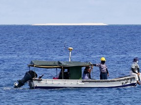 FILE - In this April 21, 2017 file photo, engineers from NAMRIA, the central mapping agency of the Philippine Government, survey the area around the Philippine-claimed Thitu Island with a sandbar sitting on the horizon off the disputed South China Sea in the western Philippines. An official says the Philippines has protested the presence of about 275 Chinese vessels that were sighted from January to March near a Philippine-occupied island in the disputed South China Sea.