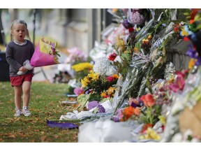 FILE - In this March 17, 2019, file photo, a girl carries flowers to a memorial wall following the mosque shootings in Christchurch, New Zealand. New Zealand's parliament on Wednesday passed sweeping gun laws which outlaw military-style weapons, less than a month after the nation's worst mass shooting left 50 dead and 39 wounded in two mosques in the South Island city of Christchurch.