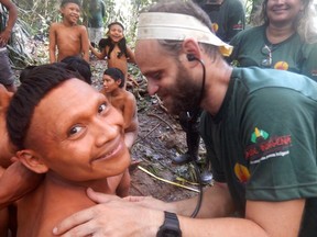 In this 2019 handout photo released by Brazil's National Indian Foundation, or FUNAI, a Korubo man smiles up at the camera as a FUNAI member checks his heart rate during an expedition to the Javari Valley, in Brazil.