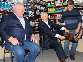 Ontario Premier Doug Ford and Vic Pettella of Vic's Shoe Repair in North Bay watch as Nipissing MPP and Ontario Finance Minister Vic Fedeli pulls on his budget boots, at Vic's Shoe Repair in North Bay.