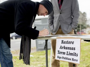 FILE - In this Jan. 18, 2016 file photo, Stuart Rubio, left, signs a petition to limit lawmakers terms in Little Rock, Ark. Arkansas was one of the first states to cap how long someone can serve in the Legislature nearly three decades ago, but competing term limit measures on the ballot next year could test just how far voters are willing to go in limiting lawmakers' time in office. In the legislative session that just wrapped up, Arkansas lawmakers sent voters a proposal that would rework the term limits on House and Senate members for the second time in the past several years.