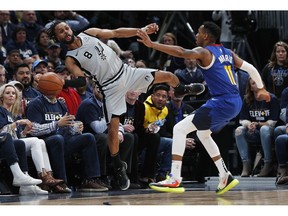 San Antonio Spurs guard Patty Mills, left, reaches out to save a ball from going out of bounds as Denver Nuggets guard Monte Morris defends in the second half of Game 1 of an NBA first-round basketball playoff series, Saturday, April 13, 2019, in Denver. The Spurs won 101-96.