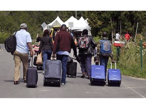 A family from Haiti approach a tent in Saint-Bernard-de-Lacolle, Quebec, stationed by Royal Canadian Mounted Police, as they haul their luggage down Roxham Road in Champlain, N.Y., on August 7, 2017. Refugee advocates are crying foul over the Trudeau government's proposed changes to immigration laws that aim to stem the flow of asylum seekers who have been crossing into Canada at unofficial border crossings. Law experts at the Canadian Association of Refugee Lawyers say the changes would strip away human rights protections from vulnerable refugee claimants.