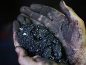 A coal miner, holds coal running through a processing plant in Welch, W.Va. on Oct. 6, 2015. An environmental group is calling on the Nova Scotia government to do more to phase out coal-fired electrical plants despite the province's exemption from the 2030 federal deadline for a national phase out.
