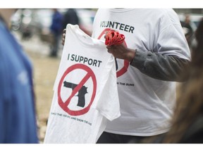 Physicians and health workers protesting in Toronto, walk past a volunteer from the anti-gun group "Silence the Violence and Shun the Guns," on Wednesday, April 3, 2019. A newly released summary of federal consultations says Canadians have wildly diverging views on banning handguns and assault-style firearms.