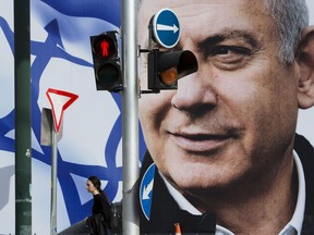 File - In this Thursday, March 28, 2019 file photo, a woman walks by an election campaign billboard showing Israel's Prime Minister Benjamin Netanyahu, the Likud party leader, in Tel Aviv, Israel. An Israeli watchdog said Monday that it's found a network of social media bots disseminating messages in support of Netanyahu ahead of next week's elections.