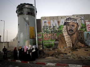 File - In this Friday, Aug. 13, 2010 file photo, Palestinian women wait near a section of Israel's separation barrier covered in graffiti, one depicting the late Palestinian leader Yasser Arafat, at the Qalandiya checkpoint , between Jerusalem and the West Bank city of Ramallah. Israel's election this month may have dimmed hopes for a two-state solution with the Palestinians as a way of resolving one of the Middle East's most intransigents conflicts. The vote, in which Prime Minister Benjamin Netanyahu coasted to another victory, left no doubt that peace talks with the Palestinians won't be on the agenda anytime soon.