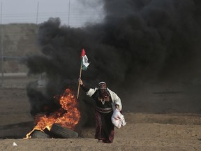 FILE - In this Oct. 5, 2018 file photo, a Palestinian woman carries a Palestinian flag during a protest at the Gaza Strip's border with Israel. Hamas controls Gaza more tightly than ever, despite unprecedented domestic unrest and its failure to significantly weaken Israel's chokehold of the territory after a year of weekly anti-blockade rallies along their shared frontier.