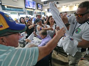 Venezuelans vie for T-shirts as they watch televised news from their country at the El Arepazo Doral Venezuelan restaurant, Tuesday, April 30, 2019, in Doral, Fla. Venezuelan opposition leader Juan Guaidó took to the streets with a small contingent of heavily armed troops early Tuesday in a bold and risky attempt to lead a military uprising and oust socialist leader Nicolas Maduro.