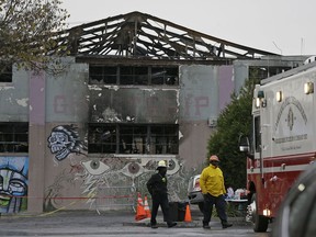 FILE - In this Dec. 7, 2016, file photo, Oakland fire officials walk past the remains of the Ghost Ship warehouse damaged from a deadly fire in Oakland, Calif. More than two years after 36 people died in the fire, Derick Almena and Max Harris, the two men who face charges of involuntary manslaughter, will stand trial on charges that they allegedly illegally converted the industrial building into an unlicensed entertainment venue and artist live-work space.