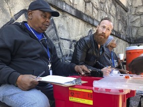 In this March 20, 2019 photo, Harry Ethridge, client services manager at the Atlanta Harm Reduction Coalition, and Jonathan Spuhler, an outreach coordinator for Absolute Care and volunteer at AHRC, set up a needle exchange station for drug users to swap out used syringes for clean syringes on English Avenue, in Atlanta.