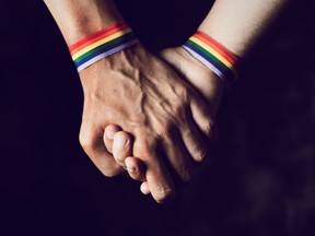 Two men hold hands, wearing rainbow-coloured bands on their wrists.