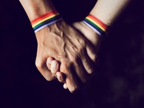 Closeup of two caucasian men holding hands with a rainbow-patterned wristban on their wrists. Forcing transgender teens to undergo psychiatric assessments before prescribing them hormone treatment is “dehumanizing” and unjustified, argues transfeminine bioethicist Florence Ashley, of McGill University.