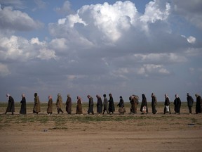 FILE - In this Friday, Feb. 22, 2019 file photo, men walk to be screened after being evacuated out of the last territory held by Islamic State group militants, near Baghouz, eastern Syria. The U.S.-led coalition says it has supported its Kurdish-led Syrian allies during an "incident" in a prison in northeastern Syria where Islamic State militants attempted to escape.