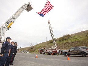 Firefighters from Pullman , Wash., left, and Colfax, Wash., line Highway 26 while a procession of law-enforcement vehicles pass under a flag on Tuesday, April 23, 2019, in Colfax, Wash. The vehicles were traveling to Portland, Ore., for a memorial service for Cowlitz County Sheriff's Deputy Justin DeRosier, was fatally shot on April 13. A memorial service for DeRosier will be held at 1 p.m. Wednesday, April 24 in Portland, Ore.