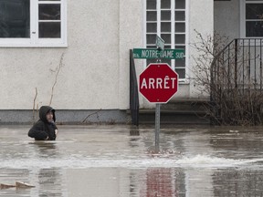 A man hops in the water of a flooded street to get to a house on Saturday, April 20, 2019 in Ste-Marie Que. Flooding in the Beauce region has halted production of some popular Quebec treats. Weekend floods struck a number of homes and buildings in Ste-Marie, Que., including the original Vachon bakery, which makes such snack cakes as Jos. Louis, Ah Caramel! and Passion Flakies.