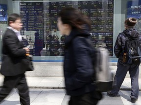 People walk by an electronic stock board of a securities firm in Tokyo, Tuesday, April 2, 2019. Asian stock prices followed Wall Street higher on Tuesday on encouraging global economic data.