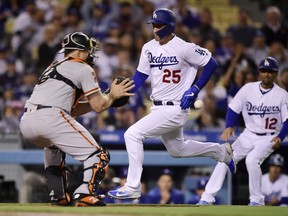 Los Angeles Dodgers' David Freese, center, scores on a single by Cody Bellinger as San Francisco Giants catcher Erik Kratz, left, takes a late throw while third base coach Dino Ebel watches during the first inning of a baseball game Wednesday, April 3, 2019, in Los Angeles.