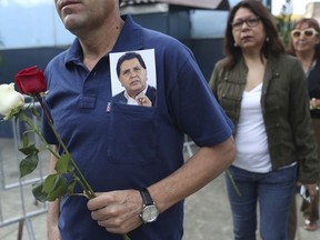 A man wearing a photograph of Peru's late President Alan Garcia arrives to Garcia's political party headquarters where his wake is taking place in Lima, Peru, Friday, April 19, 2019. Garcia shot himself in the head and died Wednesday as officers waited to arrest him in a massive graft probe that has put the country's most prominent politicians behind bars and provoked a reckoning over corruption.