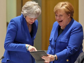 Prime minister Theresa May (L) and Chancellor Angela Merkel laugh in Brussels on April 10, 2019, over a tablet showing the two of them speaking to their respective parliaments on Wednesday wearing similar blue jackets.