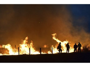 In this Sunday, April 7, 2019, photo Lame Deer, Mont., residents watch as a fire races across a field on the edge of town.