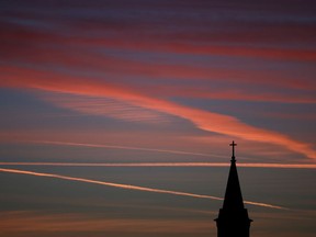 FILE - In this Saturday, Jan. 18, 2014 file photo, contrails from jets glow pink as they are illuminated by the setting sun in the skies beyond a church in Kansas. According to a Gallup poll released on Thursday, April 18, 2019, the percentage of U.S. adults who belong to a church or other religious institution has plunged by 20 percentage points over the past two decades, hitting a low of 50% last year.