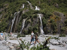 In this Feb. 7, 2016 file photo, tourists walk past waterfalls at the Franz Josef Glacier in New Zealand. The Fox and Franz Josef glaciers have been melting at such a rapid rate that it has become too dangerous for tourists to hike onto them from the valley floor, ending a tradition that dates back a century.